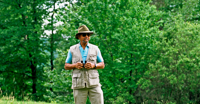 Man with binoculars with green trees in background